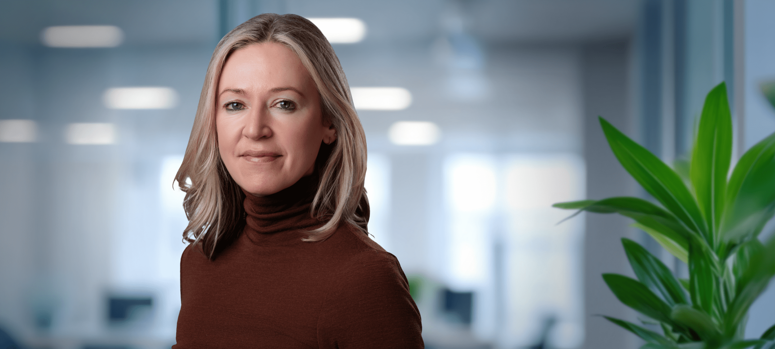 Adherent (formerly Compliance & Risks). A woman with blonde hair and a brown turtleneck smiles at the camera in a professional headshot.
