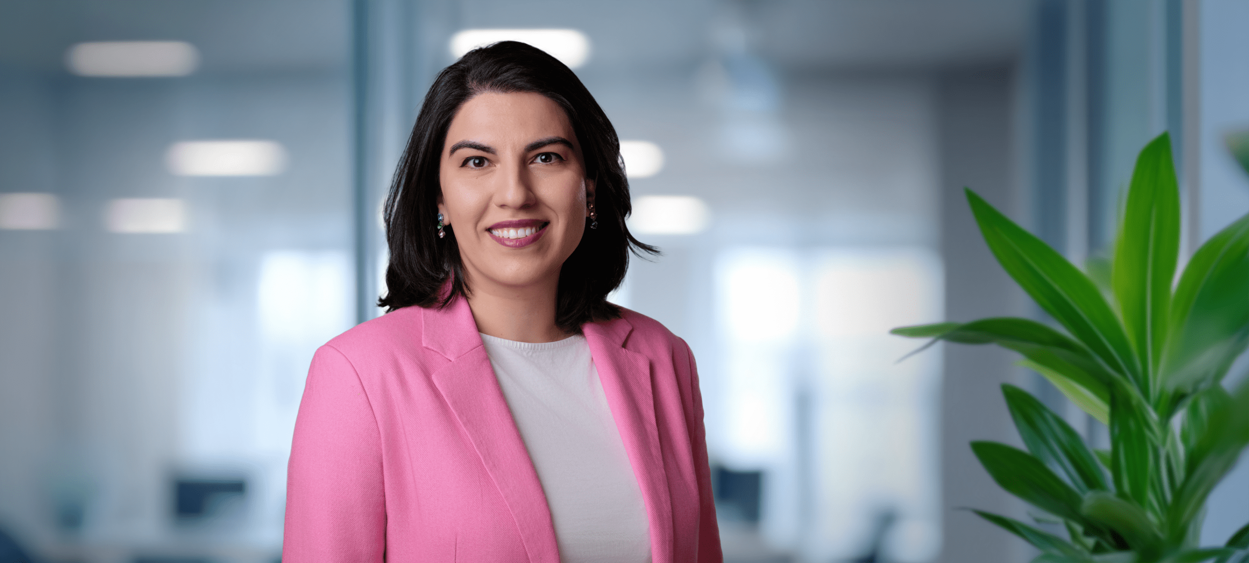 Adherent (formerly Compliance & Risks). A smiling woman with dark hair and a pink blazer in a professional office setting.