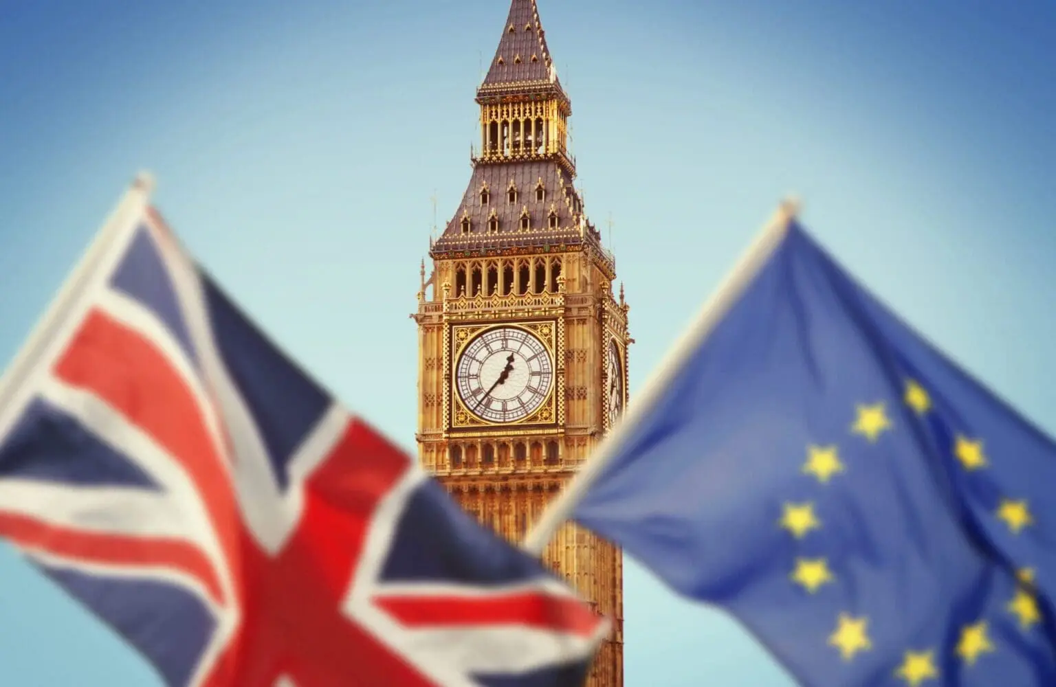 Adherent (formerly Compliance & Risks). Big Ben clock tower in focus, flanked by a blurred Union Jack flag on the left and a blurred European Union flag on the right.