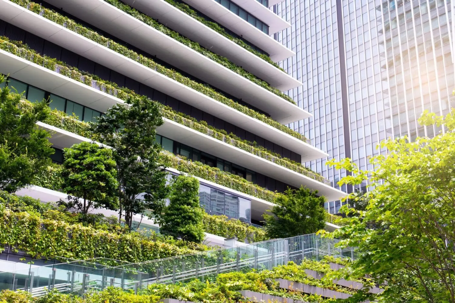 Adherent (formerly Compliance & Risks). A modern building with terraced balconies covered in lush green plants and trees, next to a reflective glass skyscraper.