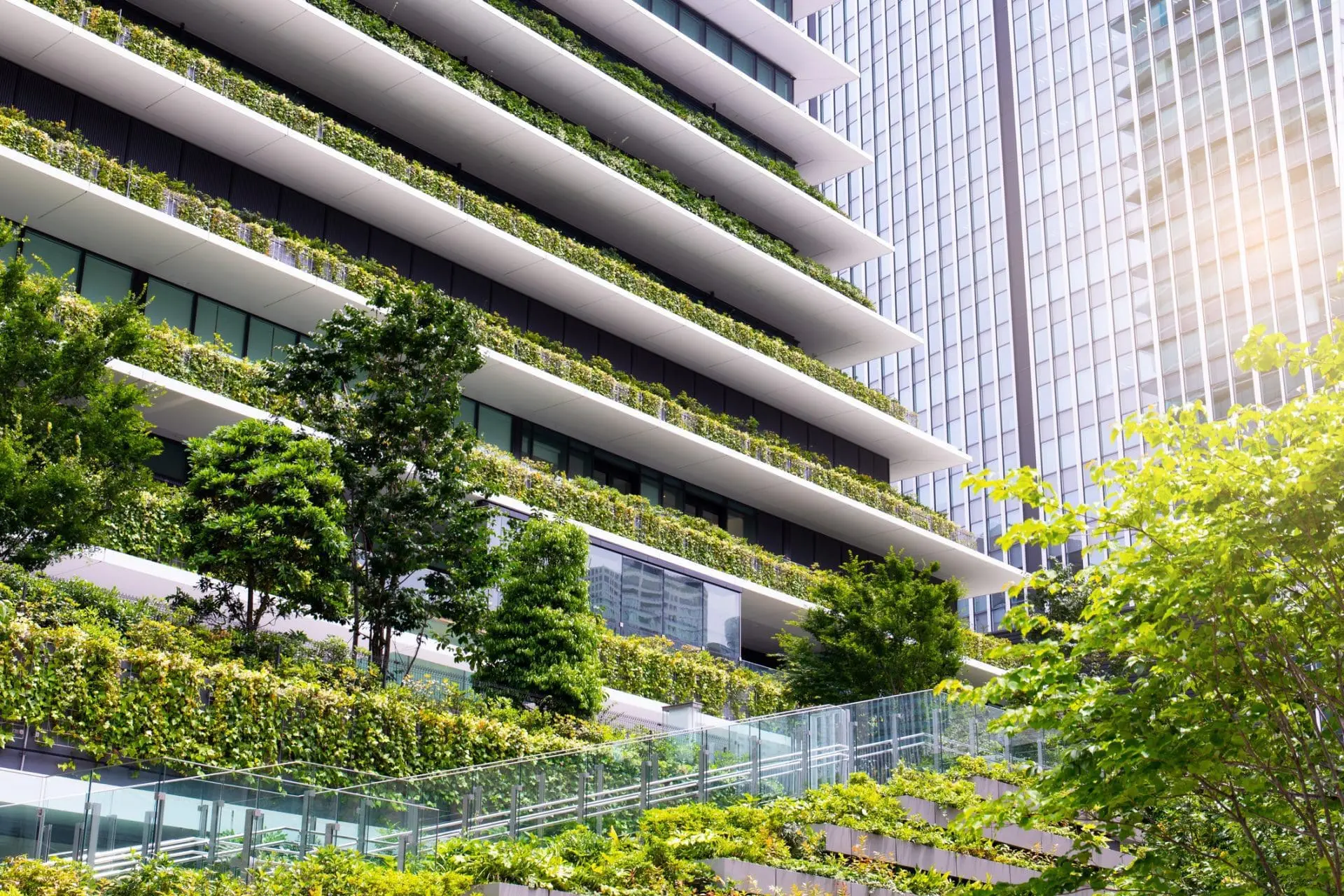 Adherent (formerly Compliance & Risks). A modern building with terraced balconies covered in lush green plants and trees, next to a reflective glass skyscraper.