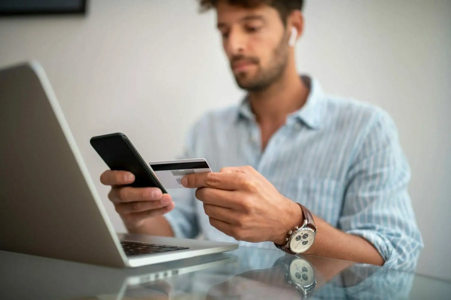 Adherent (formerly Compliance & Risks). A man holding a smartphone and a credit card, with a laptop nearby, suggesting online shopping.