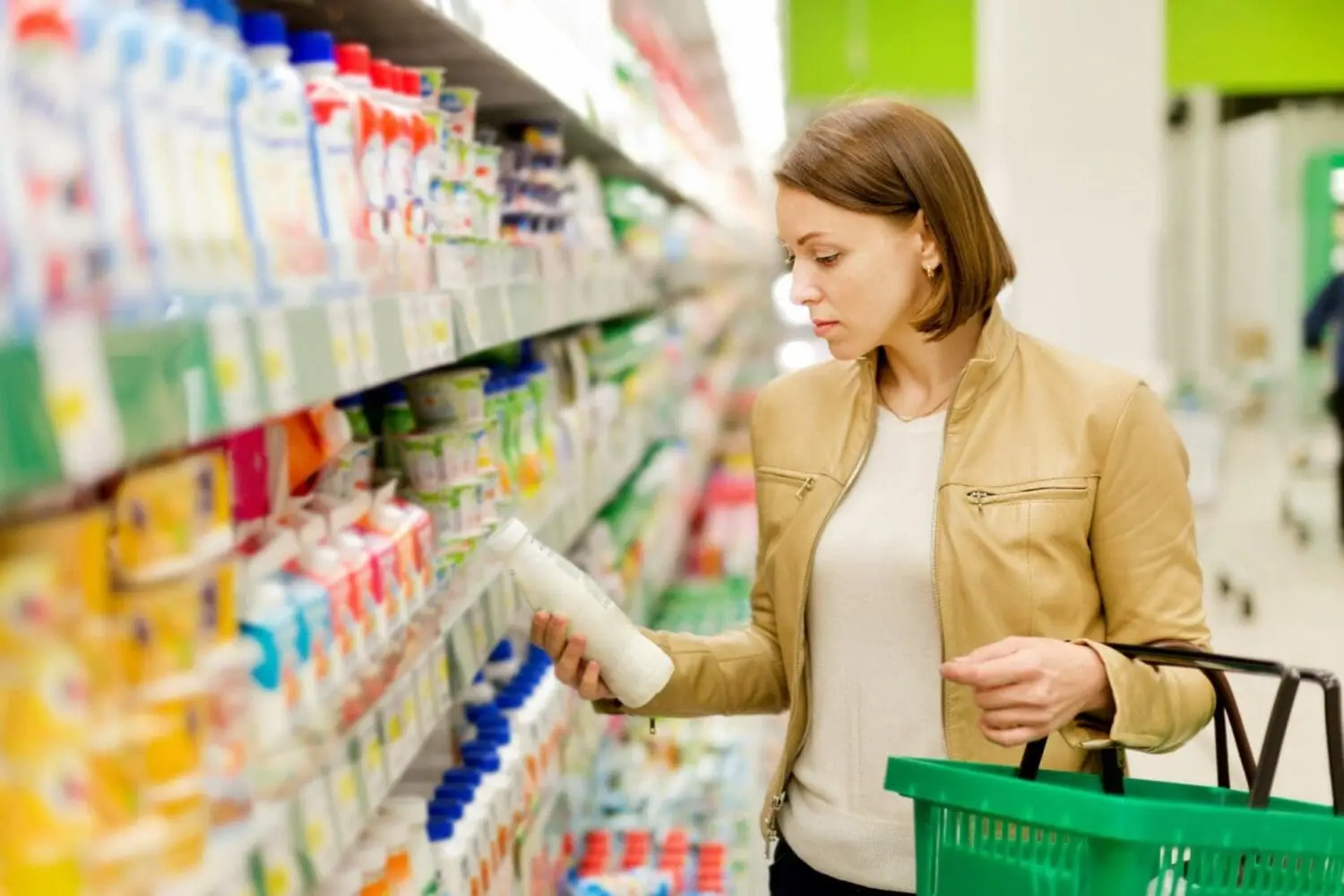 Adherent (formerly Compliance & Risks). A woman in a supermarket aisle holding a white bottle and a green shopping basket, looking at the product.