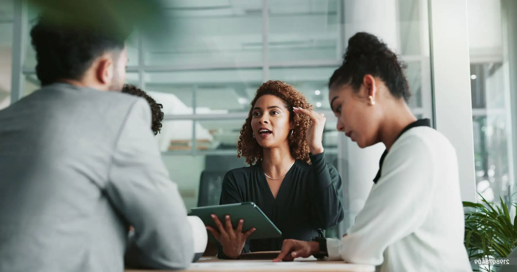 Adherent (formerly Compliance & Risks). Three professionals in a meeting. A woman in the center speaks, holding a tablet, while a man and another woman listen and interact with documents on the table.