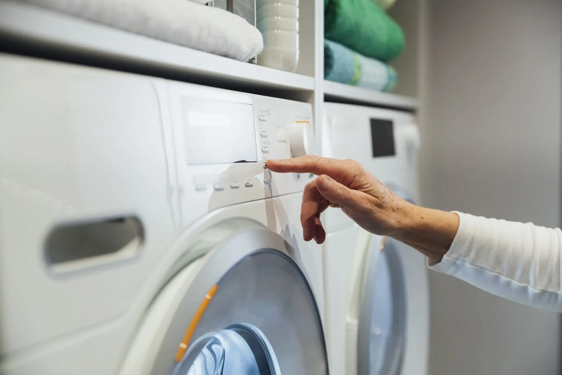 A hand pressing a button on the control panel of a white front-loading washing machine.