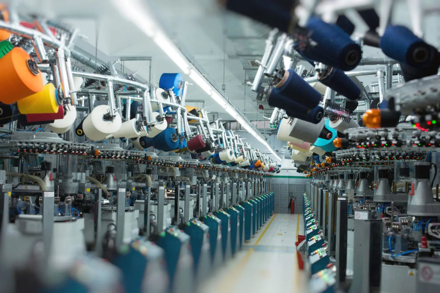 A long view of a textile factory with rows of automated machines, each loaded with numerous colorful yarn spools in various bright colors.