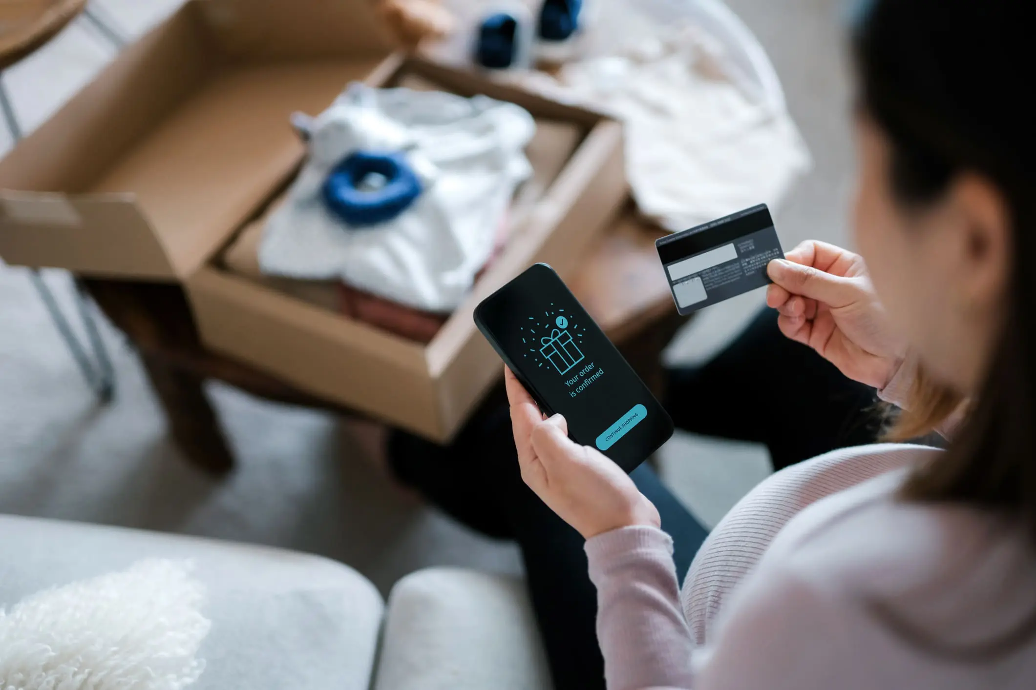 Adherent (formerly Compliance & Risks). A person holds a smartphone showing an 'order confirmed' message and a credit card, with an open box of baby items in the background.