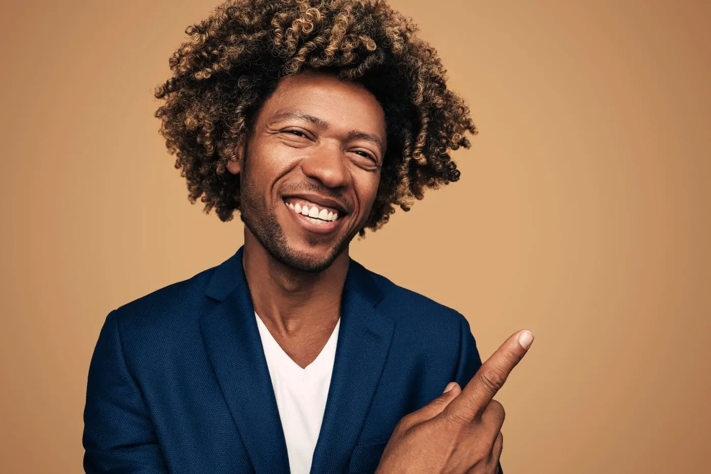 A smiling man with curly hair in a blue blazer points to the right.