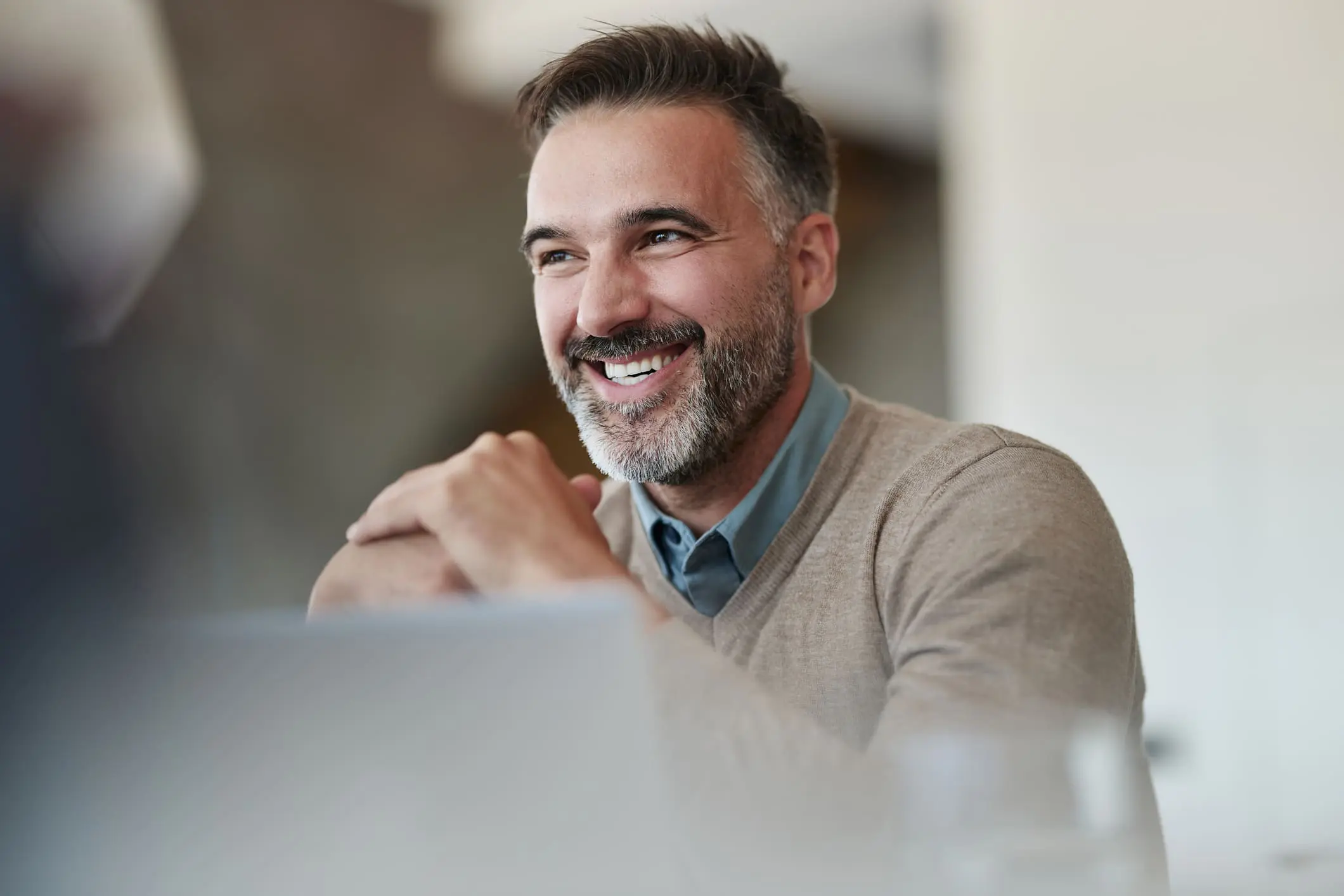Adherent (formerly Compliance & Risks). A smiling man with dark hair and a graying beard, wearing a beige sweater, looks to the side with an engaged expression.