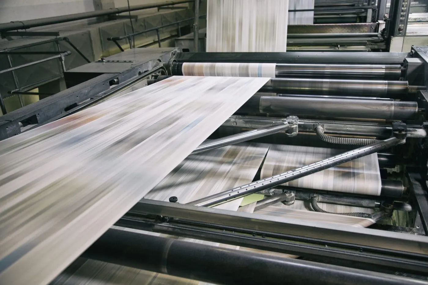 A close-up of an industrial printing press with blurred paper rapidly moving through large metal rollers, conveying high-speed production.