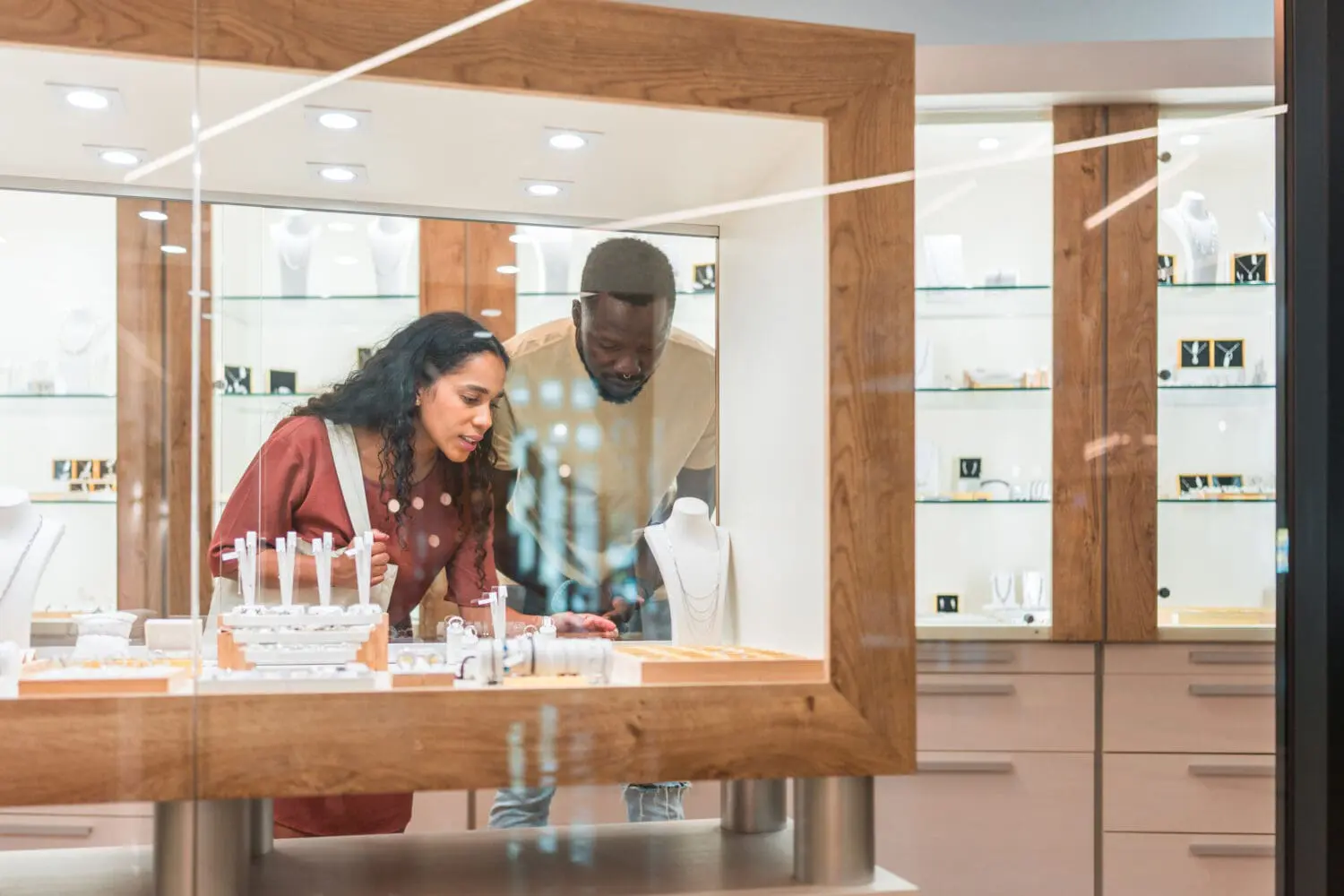 Adherent (formerly Compliance & Risks). A man and a woman looking closely at jewelry displayed in a glass case in a store.