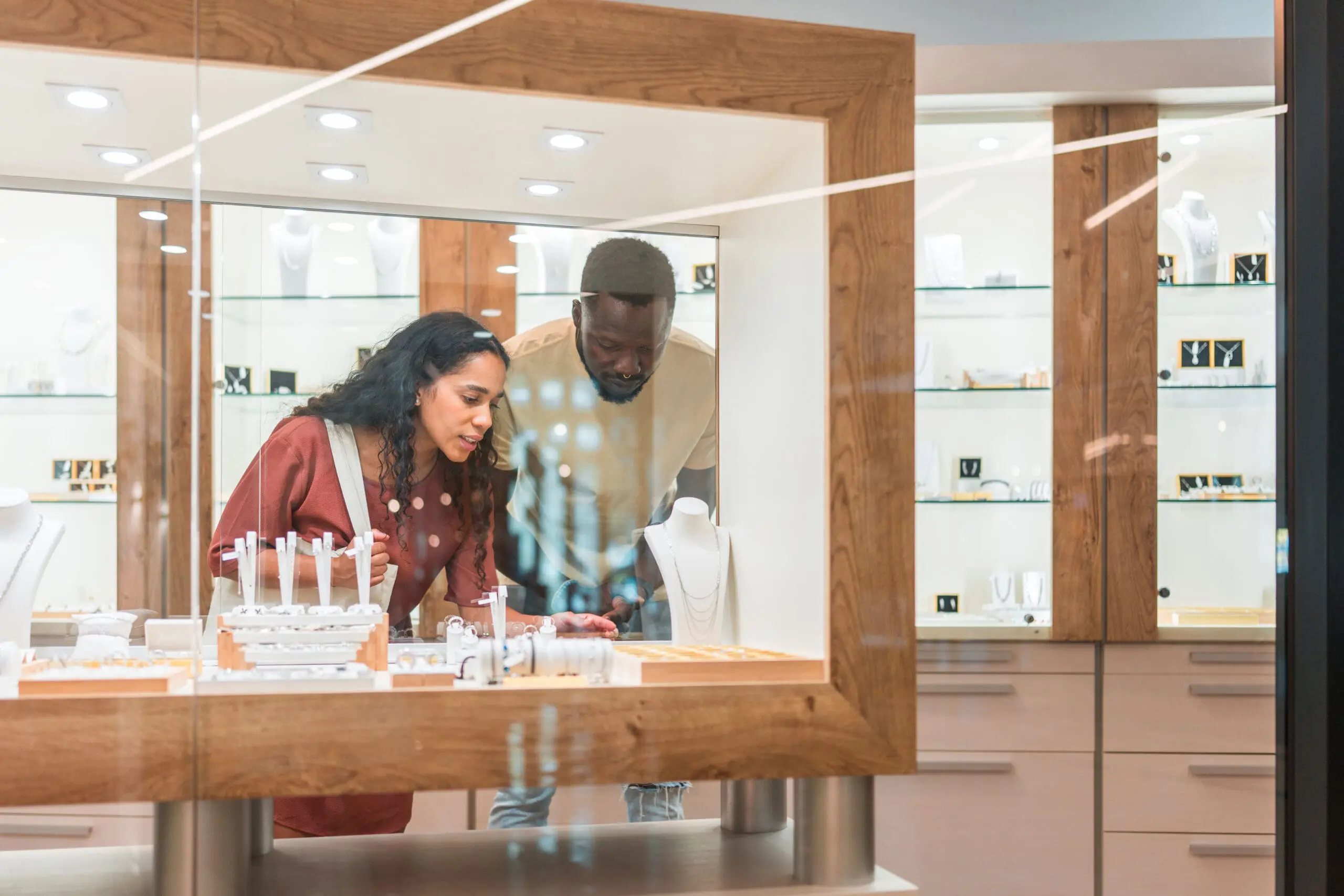 A man and a woman looking closely at jewelry displayed in a glass case in a store.
