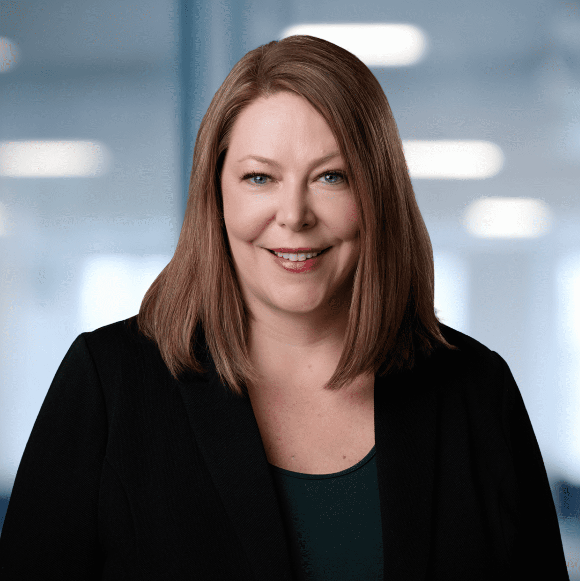 Adherent (formerly Compliance & Risks). Headshot of a smiling woman with light brown hair and blue eyes, wearing a black blazer.