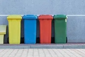 Adherent (formerly Compliance & Risks). Four colorful recycling bins (yellow, blue, red, green) lined up against a gray wall.