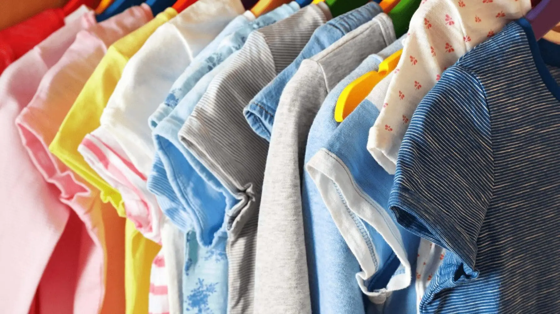 Adherent (formerly Compliance & Risks). A close-up of various colorful t-shirts hanging on hangers, including pink, yellow, blue, gray, and striped patterns.