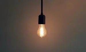 Adherent (formerly Compliance & Risks). An illuminated light bulb hanging from a black cord against a dark background.