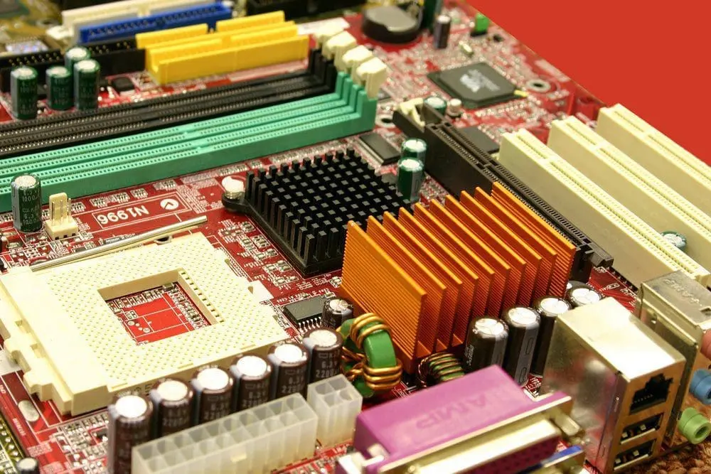 Adherent (formerly Compliance & Risks). Close-up of a red computer motherboard with various colorful slots, heatsinks, and electronic components.
