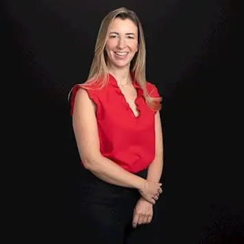 Adherent (formerly Compliance & Risks). A smiling woman with long blonde hair wearing a red sleeveless top and black pants stands against a black background.