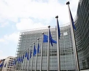 Adherent (formerly Compliance & Risks). European Union flags on flagpoles in front of a large glass building under a cloudy sky.