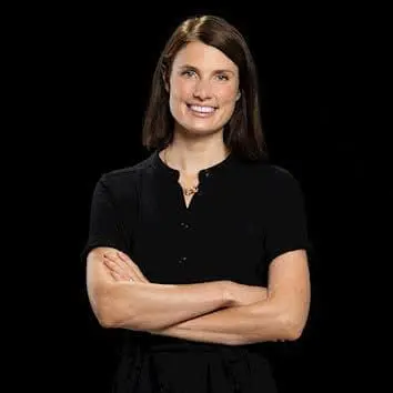 Adherent (formerly Compliance & Risks). A smiling woman with dark hair, wearing a black collared shirt with arms crossed, against a black background.