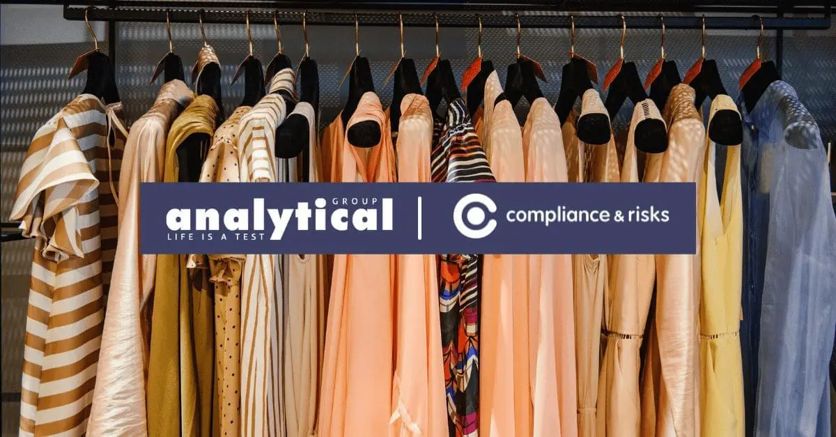 Adherent (formerly Compliance & Risks). A clothing rack displaying numerous dresses and flowing tops in shades of beige, peach, gold, and blue, with some patterned garments. A blue banner with white text 'analytical GROUP | LIFE IS A TEST | compliance & risks' is overlaid across the center.