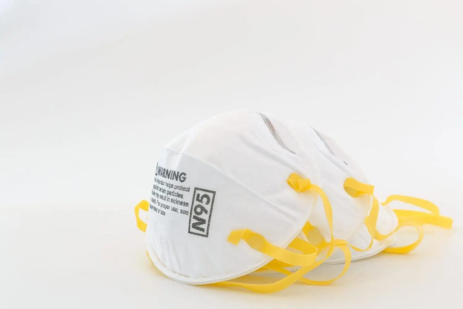 Adherent (formerly Compliance & Risks). Multiple white N95 respirator masks with yellow straps are stacked on a white background.