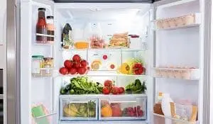 An open, brightly lit refrigerator filled with fresh fruits, vegetables, eggs, and various food containers.