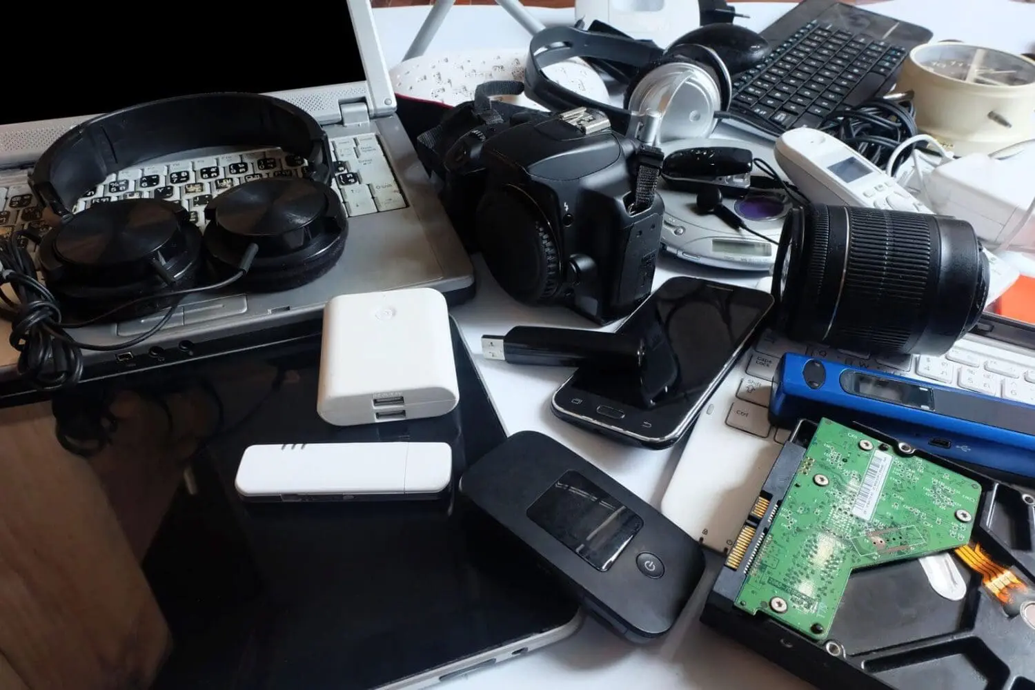 Adherent (formerly Compliance & Risks). A large, cluttered pile of various electronic devices, including laptops, headphones, cameras, smartphones, a hard drive, and other gadgets.