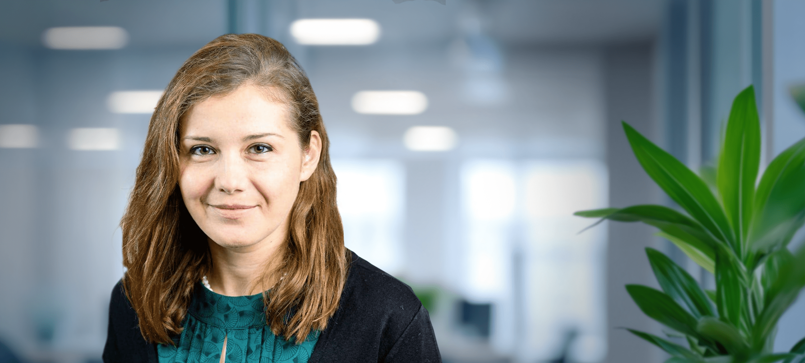 Adherent (formerly Compliance & Risks). A woman with light brown hair and a green top smiles in a blurred office environment.