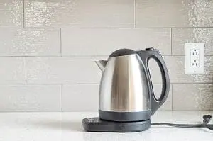 Adherent (formerly Compliance & Risks). A stainless steel electric kettle on a white countertop with a tiled backsplash and an electrical outlet.