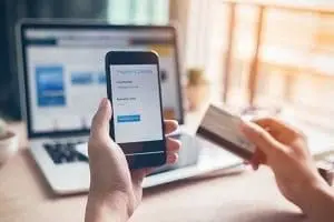 Adherent (formerly Compliance & Risks). Hands holding a smartphone displaying a payment confirmation screen and a credit card, with a laptop in the background.