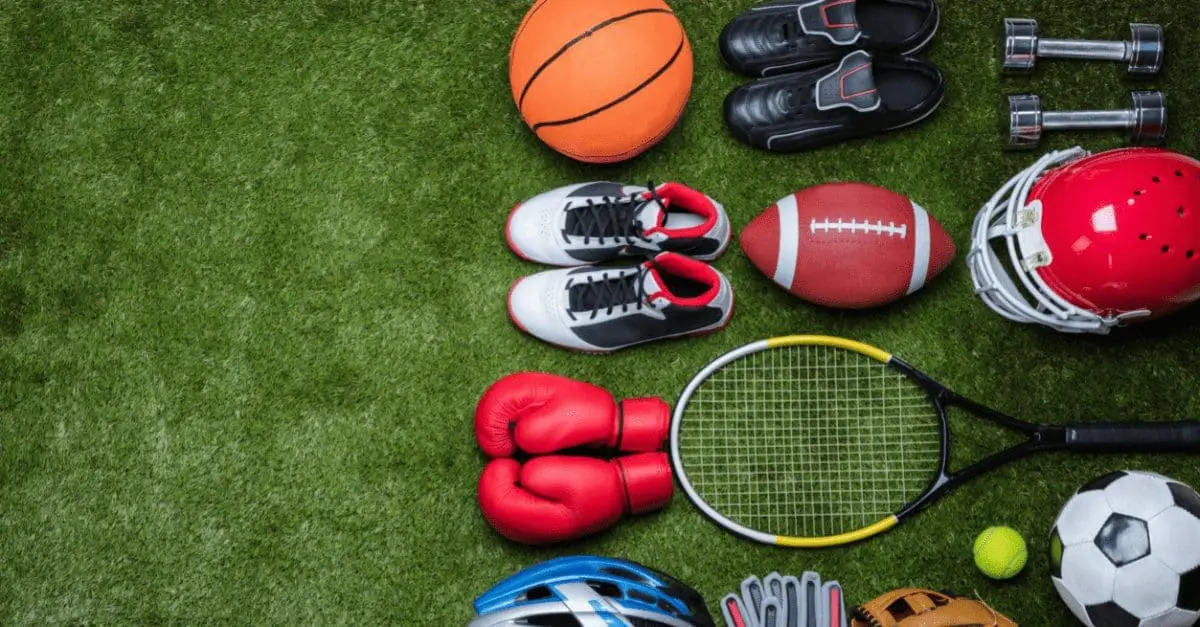 Adherent (formerly Compliance & Risks). A flat lay of various sports equipment including a basketball, football, soccer ball, tennis racket, boxing gloves, helmets, shoes, and dumbbells on green artificial grass.