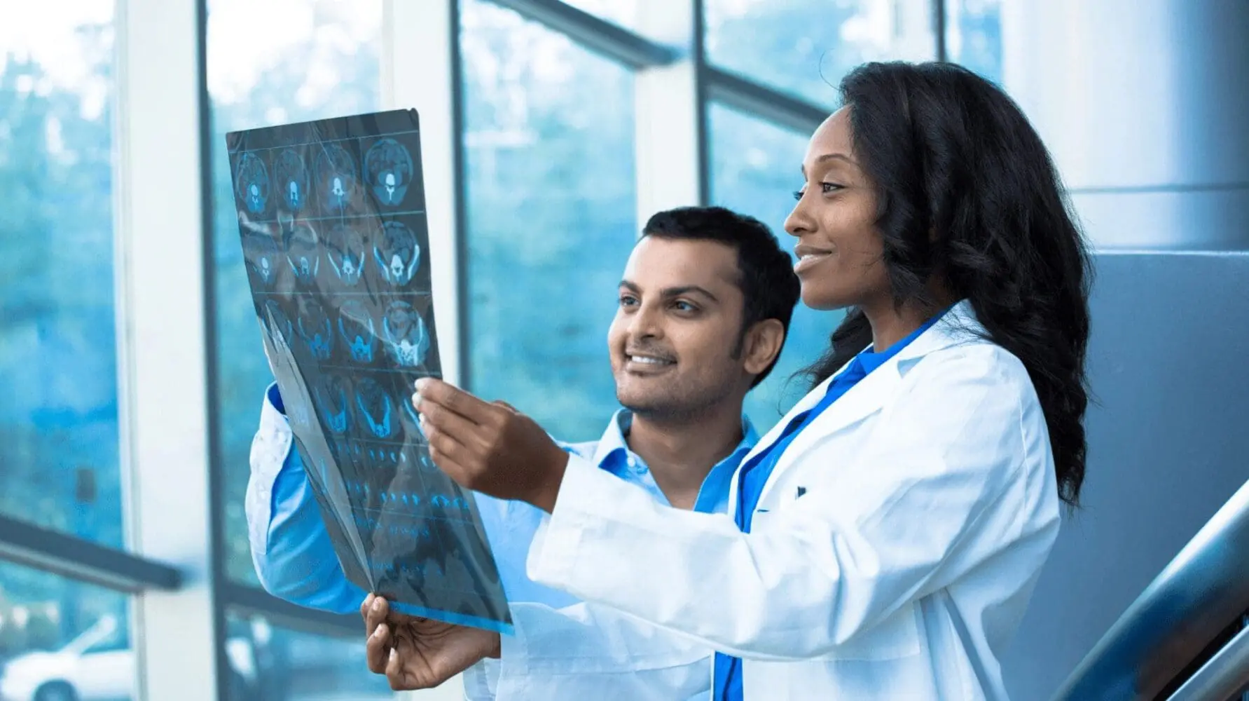 Adherent (formerly Compliance & Risks). A man and a woman, both medical professionals, examine a medical imaging film together.