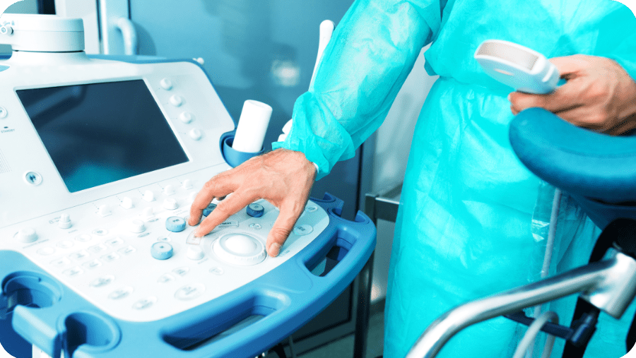 Adherent (formerly Compliance & Risks). A person in a blue-green surgical gown operates the control panel of an ultrasound machine with their hand.