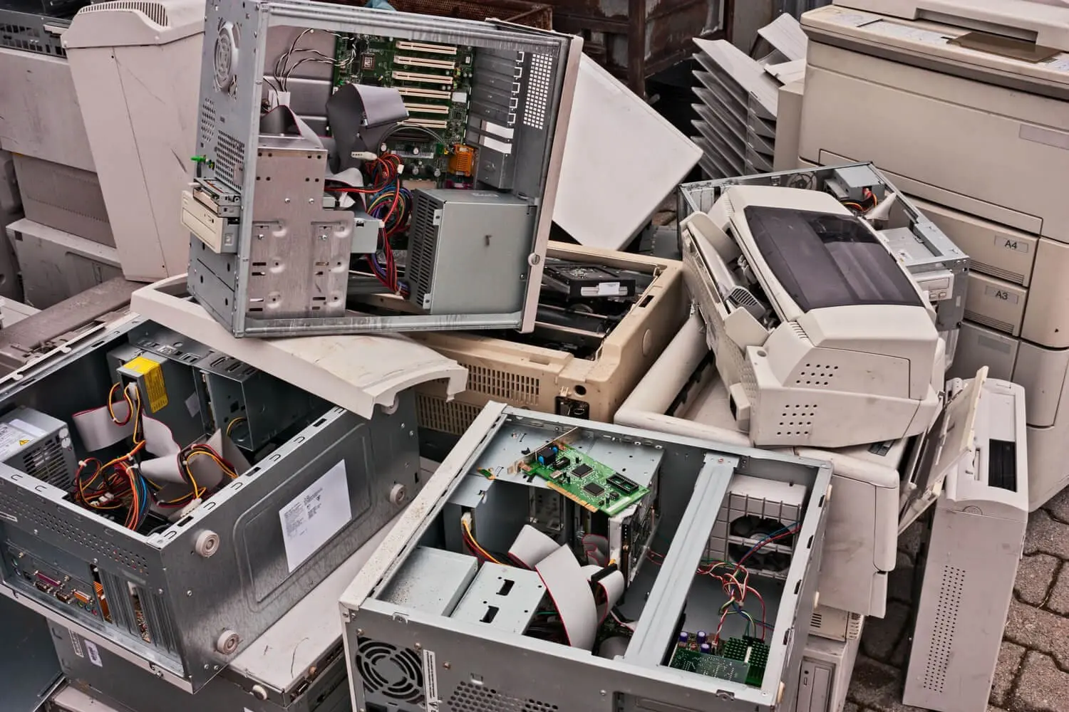 Adherent (formerly Compliance & Risks). A large pile of old, beige and gray electronic waste, including computer towers with exposed components, printers, and scanners, stacked haphazardly.