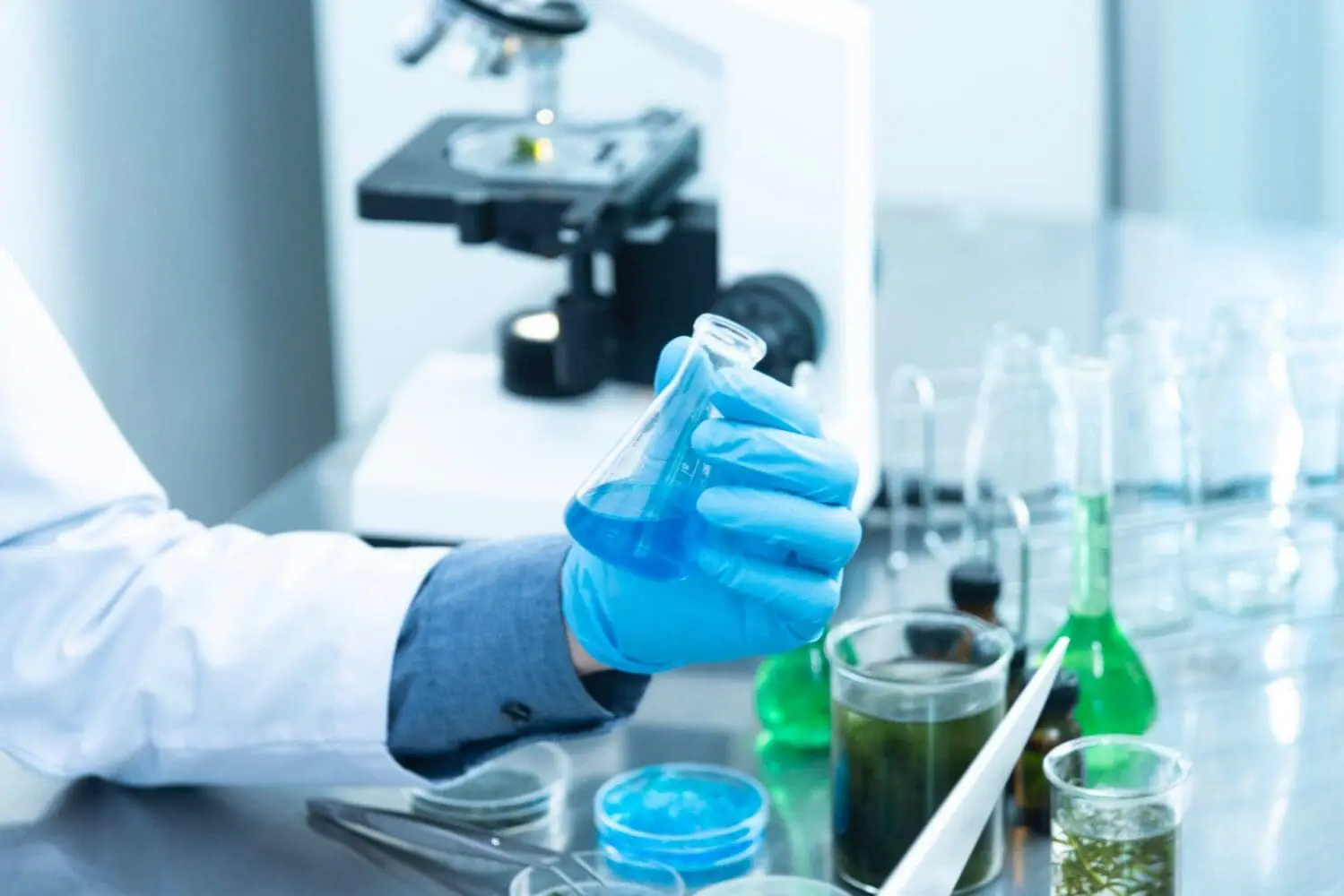 Adherent (formerly Compliance & Risks). A gloved hand holds a flask with blue liquid in a laboratory, with a microscope and other beakers visible.