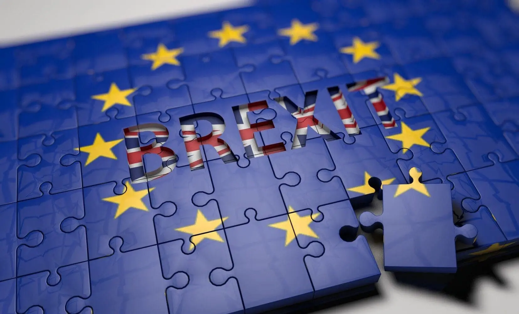A 3D puzzle depicting the EU flag with the word 'BREXIT' cut out, revealing the UK flag. One puzzle piece is detached.