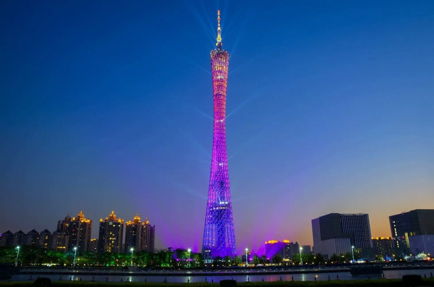 Adherent (formerly Compliance & Risks). The Canton Tower at night, illuminated in purple and pink, with city buildings and a river in the foreground.