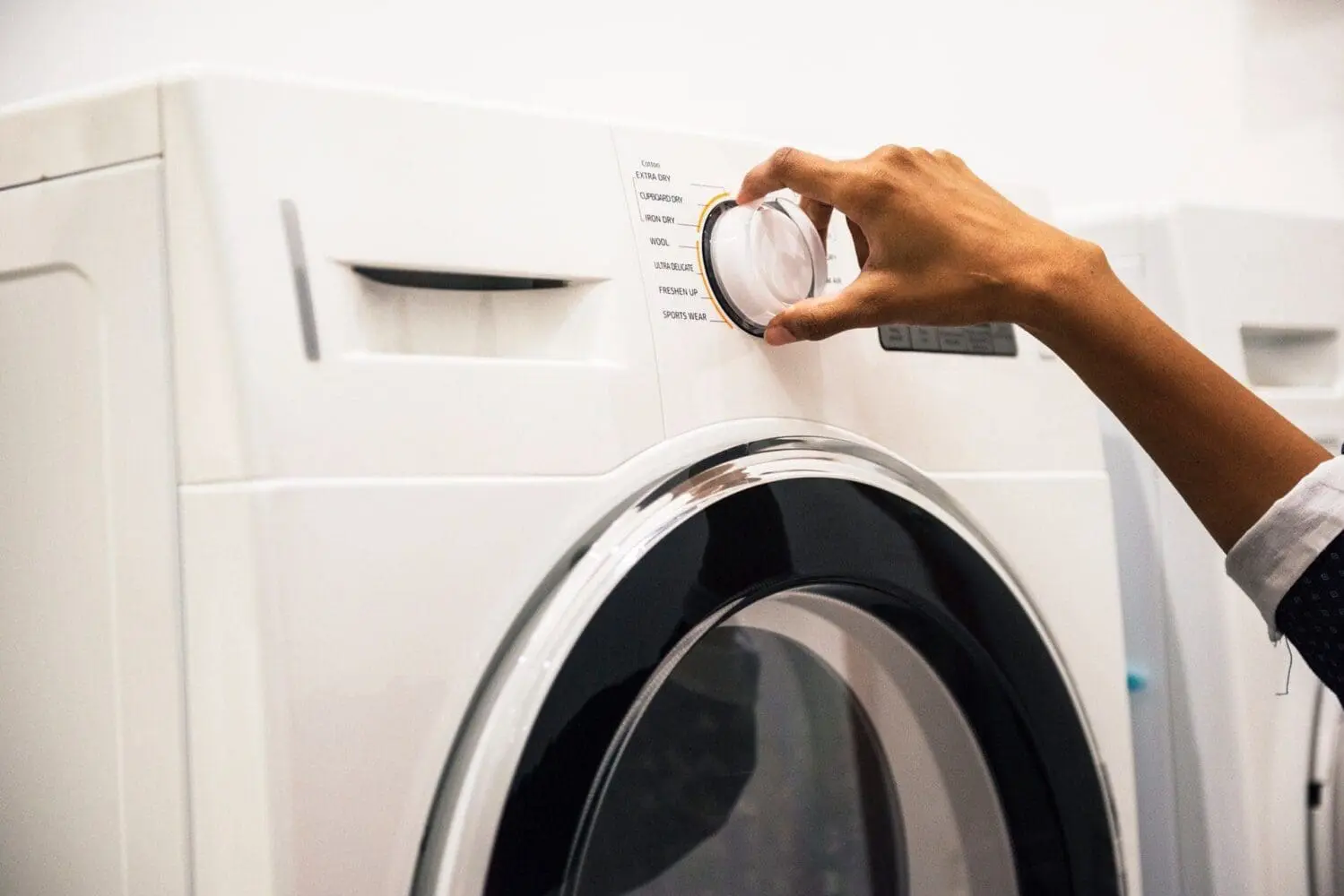 Adherent (formerly Compliance & Risks). A person's hand turns a clear dial on a white washing machine or dryer, selecting a cycle.