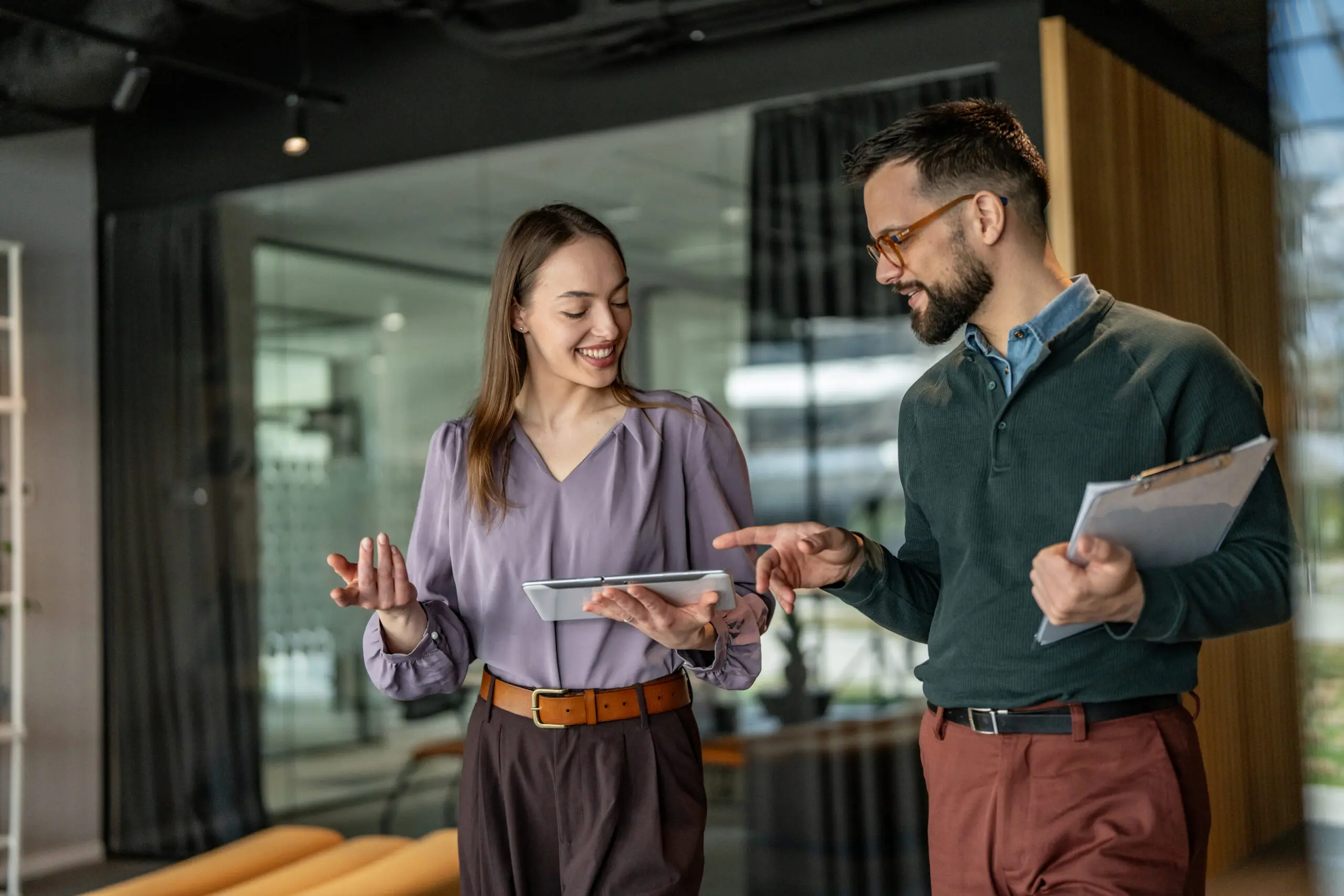 Adherent (formerly Compliance & Risks). A smiling woman and man in an office, looking at a tablet. The man points at the screen while the woman holds it.