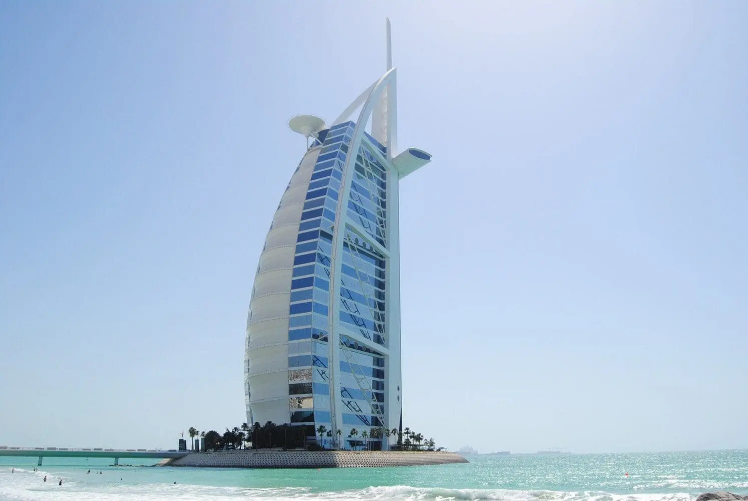 Adherent (formerly Compliance & Risks). The Burj Al Arab Jumeirah hotel, a sail-shaped skyscraper with blue glass windows, stands on an artificial island in turquoise ocean water under a clear blue sky.