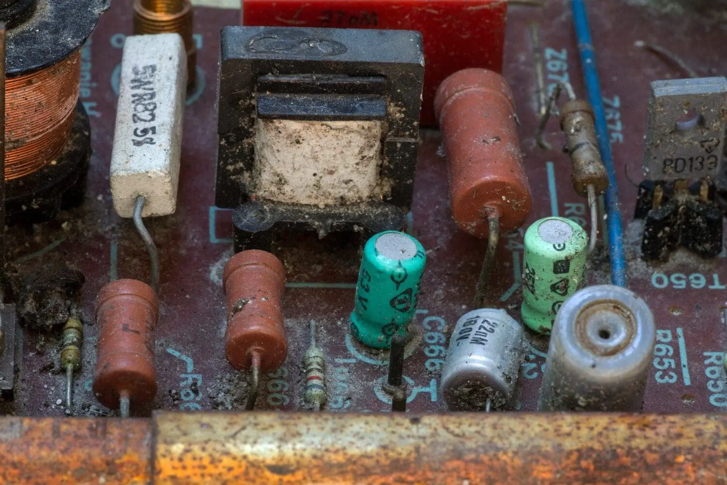 Adherent (formerly Compliance & Risks). A close-up of a very dusty, reddish-brown circuit board with various electronic components including resistors, capacitors, a coil, and a transformer.