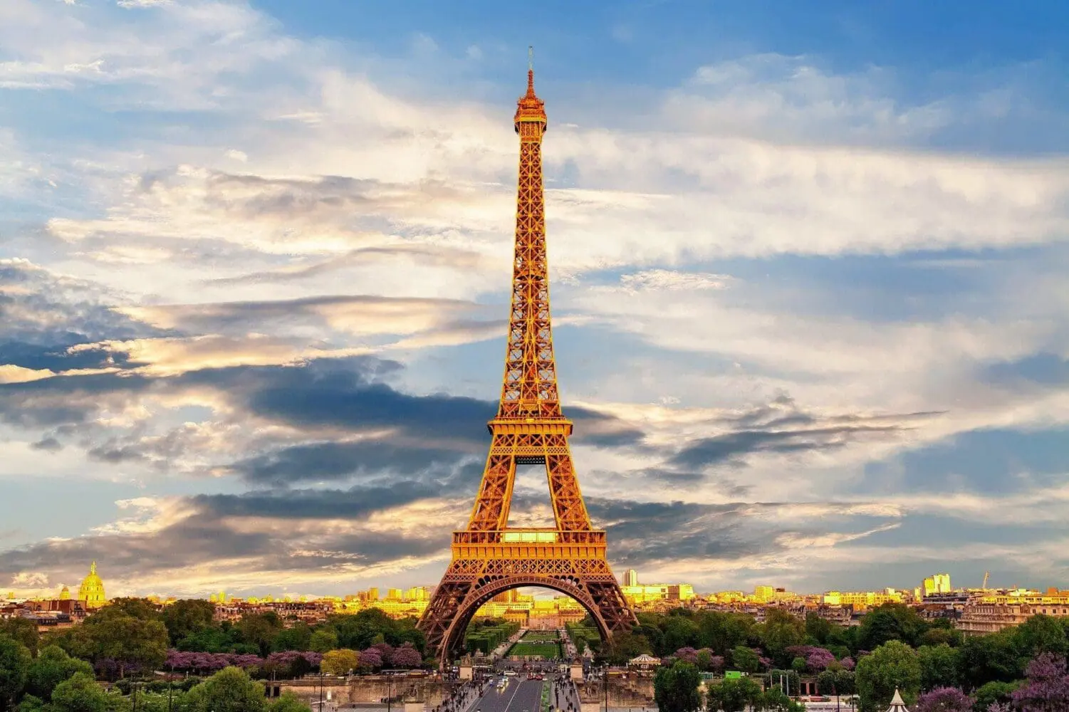 Adherent (formerly Compliance & Risks). The Eiffel Tower stands tall and golden against a dramatic, cloudy sunset sky, with the city of Paris and lush trees in the foreground.