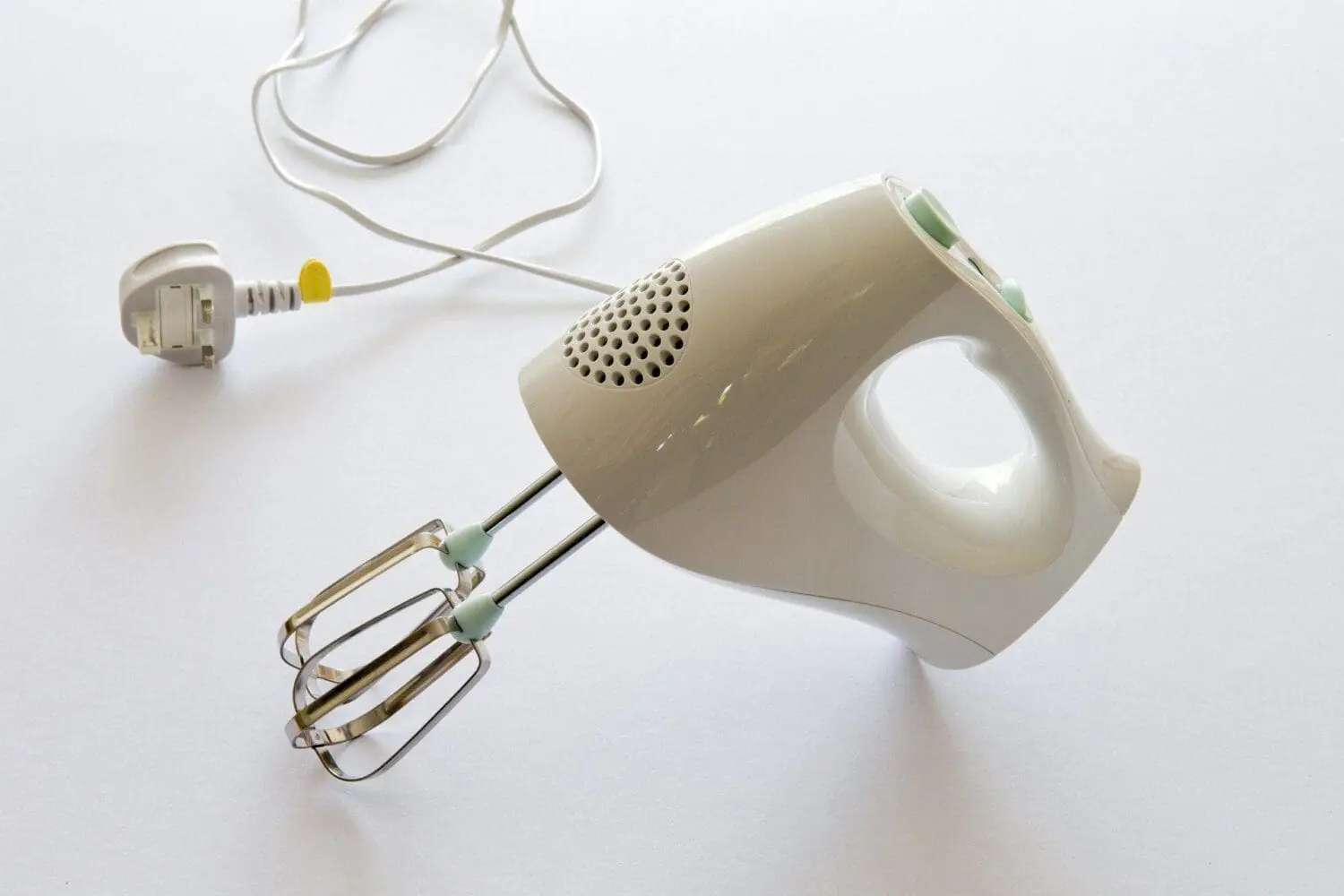 Adherent (formerly Compliance & Risks). A light beige electric hand mixer with two chrome beaters and a white power cord with a UK plug, lying on a white surface.