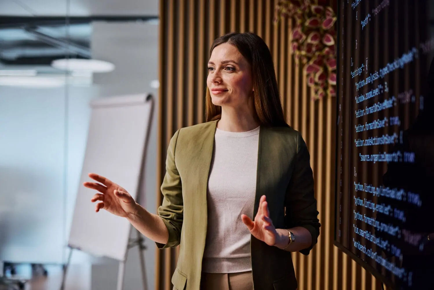Adherent (formerly Compliance & Risks). Young adult businesswoman gesturing while presenting a software project using a digital screen, showcasing innovation and technology in the workplace
