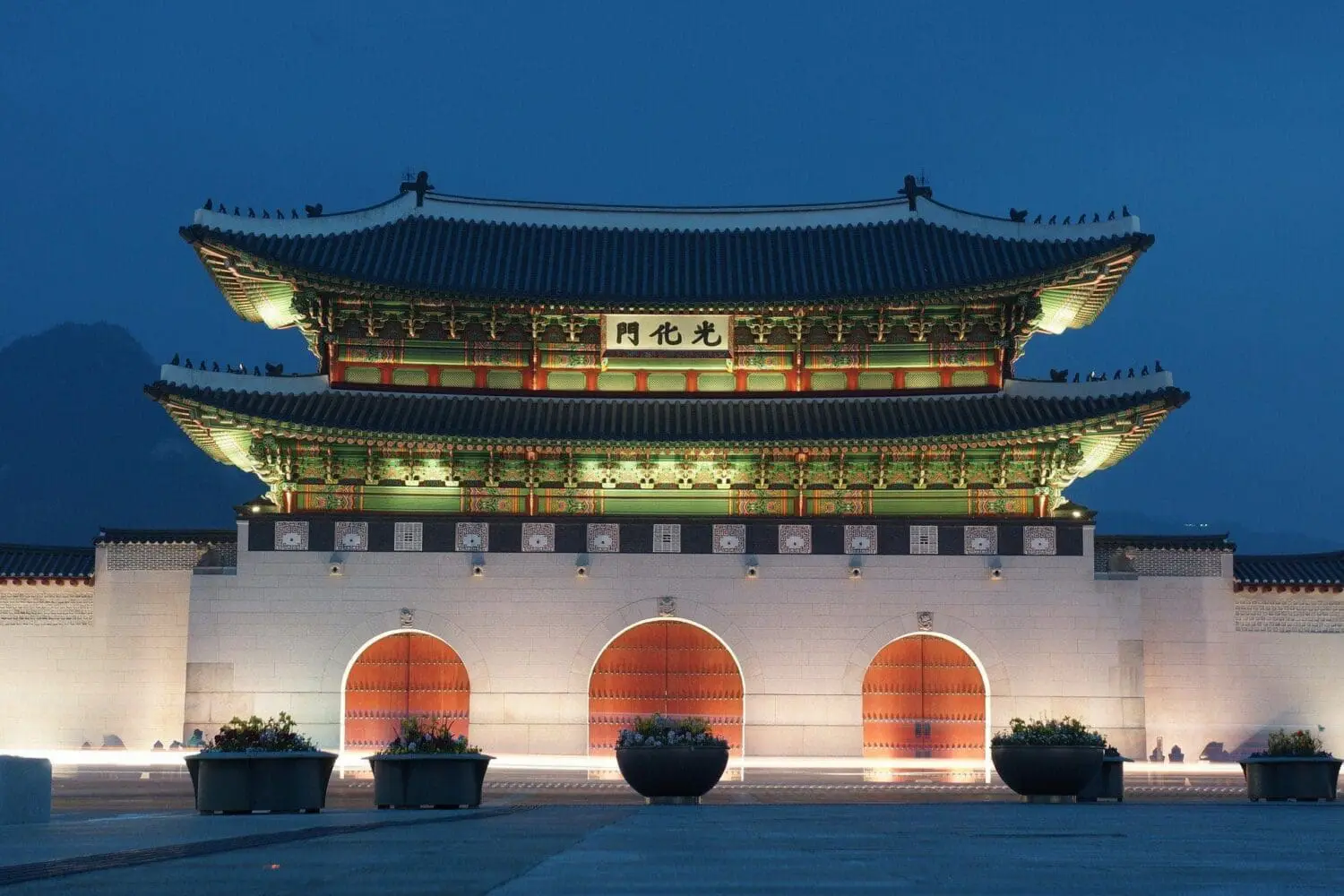 Adherent (formerly Compliance & Risks). Gwanghwamun Gate illuminated at night, featuring a multi-tiered roof, ornate eaves, and three arched wooden gates on a stone base.