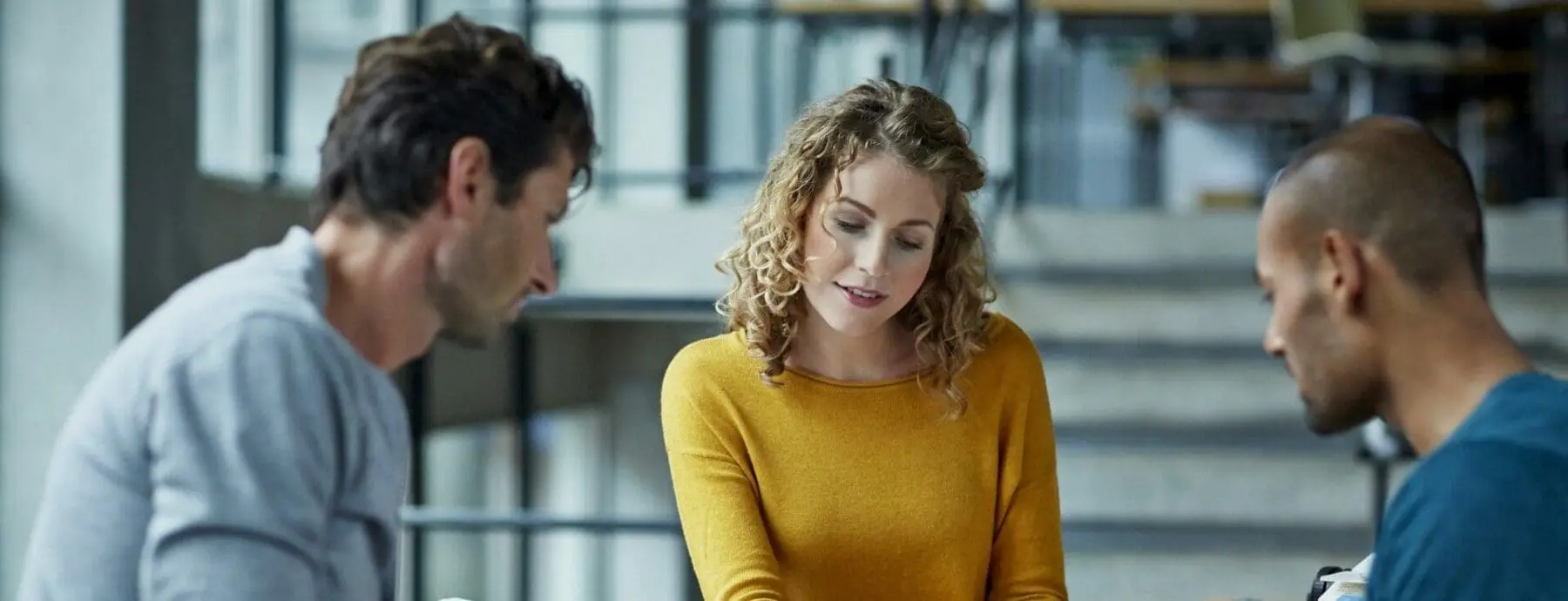 Adherent (formerly Compliance & Risks). Three people, two men and one woman, are gathered together, looking down and engaged in a discussion.