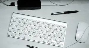 Adherent (formerly Compliance & Risks). Top-down view of a desk with a silver wireless keyboard, white wired mouse, black external device, and a stylus pen.