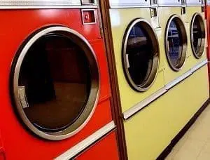 A red front-loading washing machine next to a row of yellow front-loading washing machines in a laundromat.