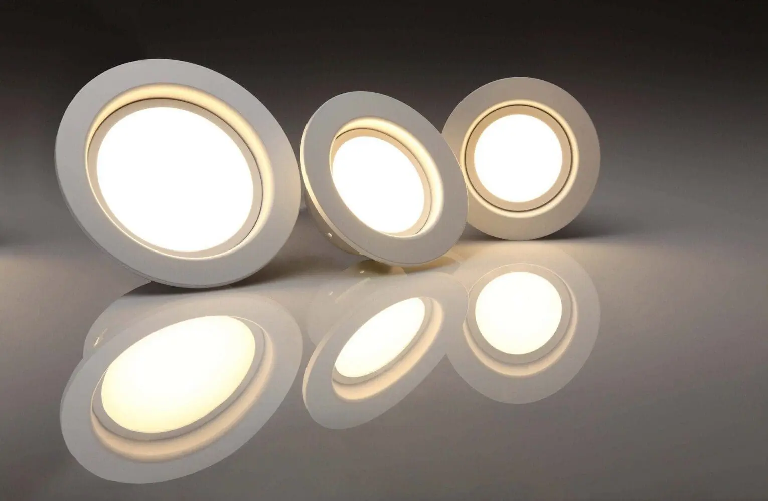 Adherent (formerly Compliance & Risks). Three illuminated white round LED lights are displayed on a reflective gray surface, showing their bright reflections.